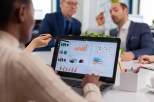Analista señalando indicadores logísticos en pantalla durante revisión de desempeño operativo con equipo